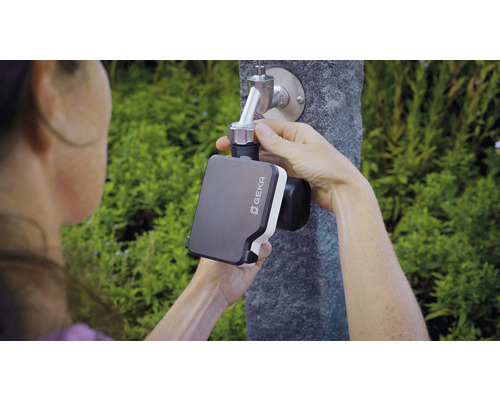 O persoană fixează un controler de irigare Geka la un robinet de grădină.