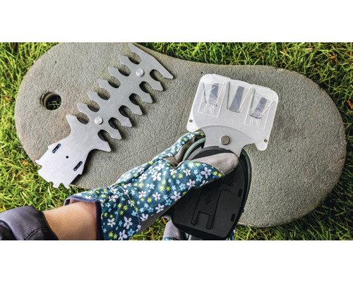 O mână cu mănușă de grădinărit ține un ascuțitor de foarfece de tuns gard viu, lângă un dispozitiv pentru alinierea foarfecelor de tuns gard viu