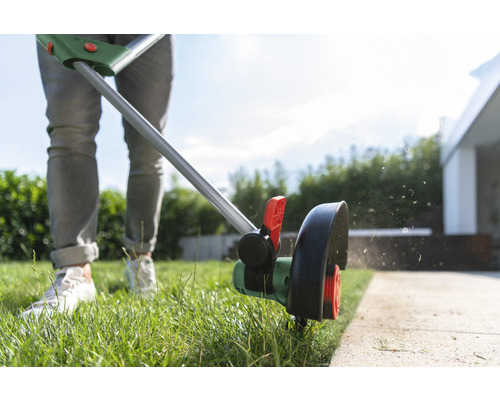 Persoană tundând gazonul cu o mașină de tuns iarba de-a lungul potecii din grădină