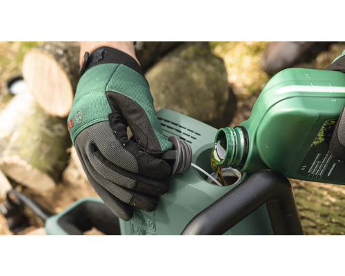 O persoană toarnă ulei într-un motoferăstrău. În fundal se văd bucăți de lemn.