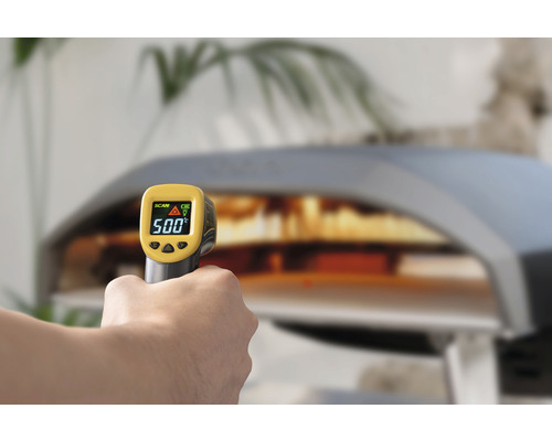 O mână ține un termometru cu infraroșu în fața unui cuptor de pizza, arătând 500 de grade.