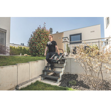 Bărbat care transportă o mașină de tuns iarba pliată pe o scară în grădină