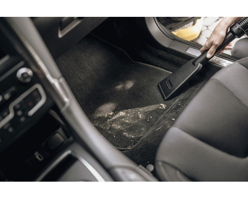 O persoană aspiră spațiul murdar pentru picioare dintr-o mașină cu un aspirator.