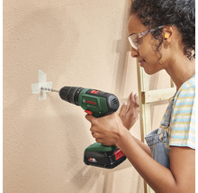 O femeie găurește un perete cu o mașină de găurit cu acumulator. Poartă ochelari de protecție.