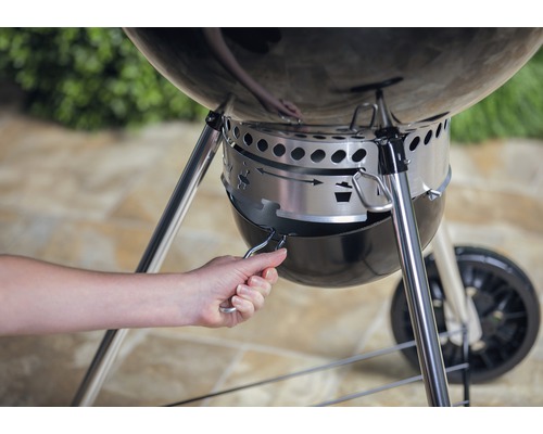 O mână acționează colectorul de cenușă al unui grătar sferic.