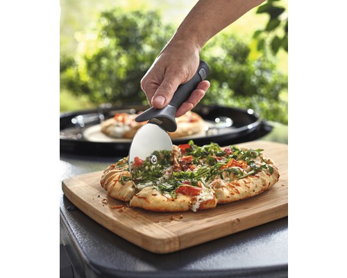 O pizza este tăiată cu un tăietor de pizza pe un tocător.