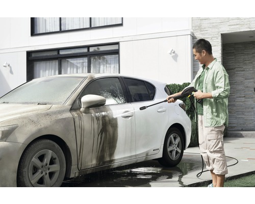 Un bărbat curăță o mașină murdară cu un aparat de spălat cu presiune în fața unei case.