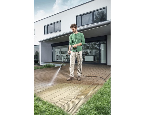 Bărbat curăță terasa de lemn cu un curățător cu presiune în fața unei case.