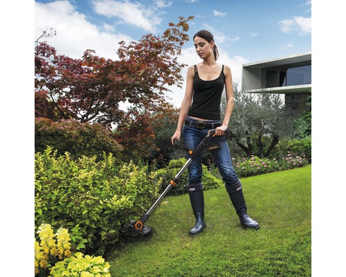 Femeie lucrează cu o mașină de tuns iarba în grădină.