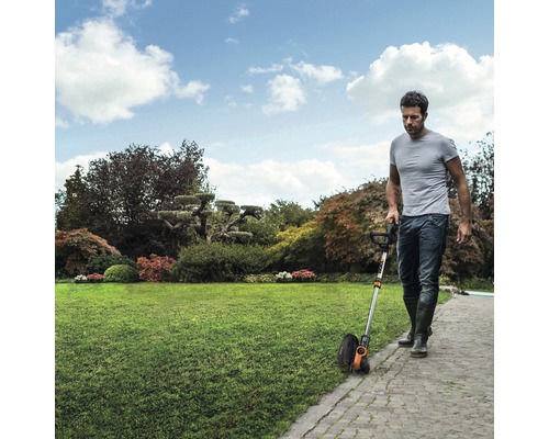 Un bărbat folosește un trimmer de gazon în grădină pentru a tăia marginile gazonului.