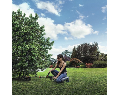 Femeie lucrează cu o mașină de tuns iarba cu acumulator în grădină, la un copac