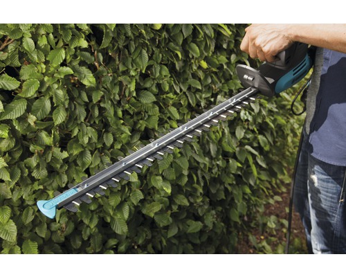 O persoană taie un gard viu cu o foarfecă electrică de tuns gard viu.