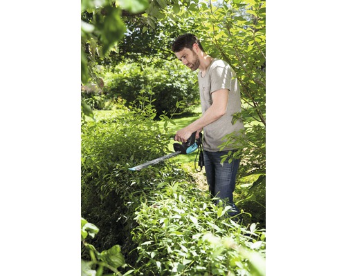 Un bărbat taie un gard viu cu o foarfecă de tuns gard viu în grădină.