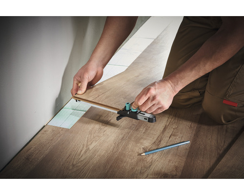 Persoană care instalează laminat cu o unealtă de marcare.