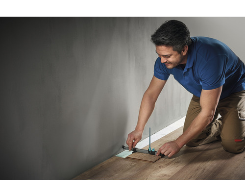 Un bărbat folosește un instrument de marcare pentru a măsura o bucată de laminat de un perete.