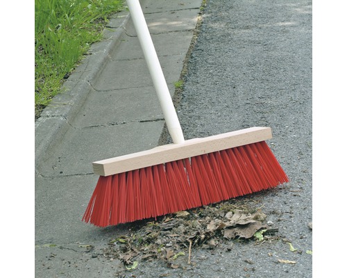 Mătură cu mâner de lemn și peri roșii măturând frunze pe asfalt