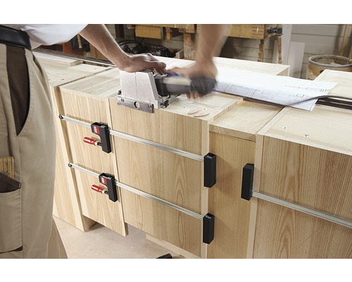 Meșterul lucrează cu o freză Lamello pe o piesă de mobilier din lemn fixată cu cleme.