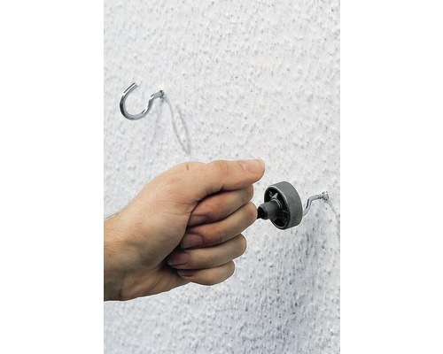 O mână înșurubează un șurub într-un perete lângă un cârlig