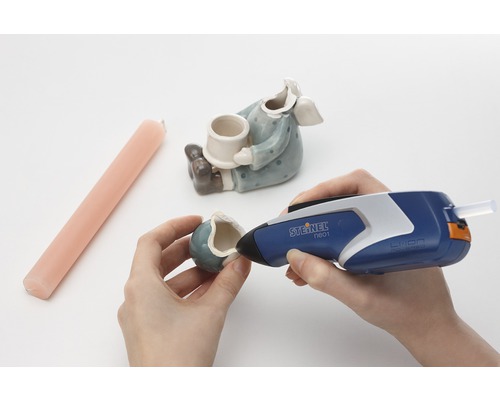 O persoană repară o figurină ceramică cu un pistol de lipit fierbinte Steinel.