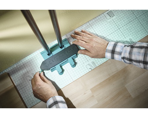 Logo Wolfcraft. O persoană folosește un șablon de marcare pentru a marca țevile de încălzire pe un substrat izolator.