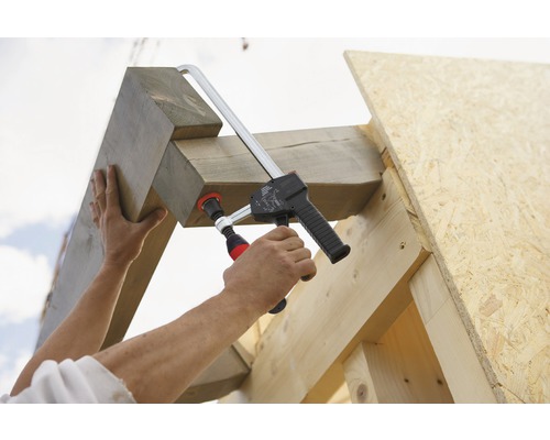 O persoană fixează grinzi de lemn pe un cadru de lemn cu o clemă.