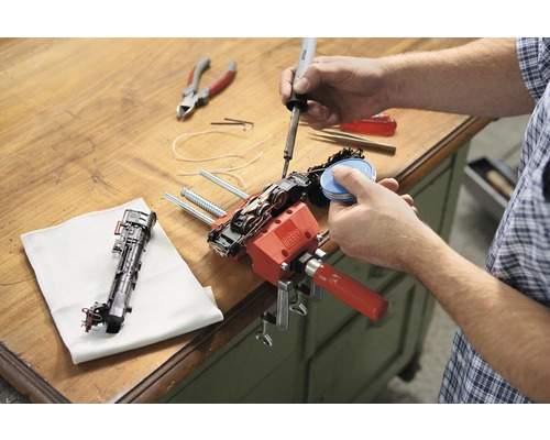 O persoană repară un model de tren cu un pistol de lipit și o menghină