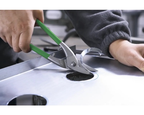 O persoană taie o gaură într-o foaie de metal cu foarfece de tablă.