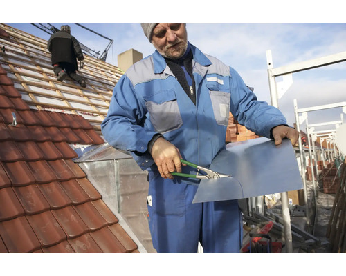 Un meșter taie o piesă de tablă pe un acoperiș cu țigle.