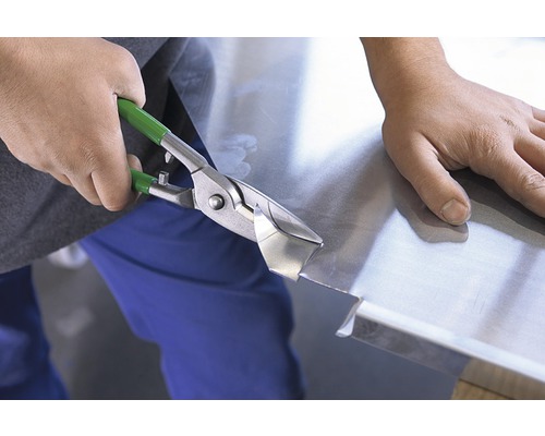 O persoană taie tablă cu foarfece de tablă.