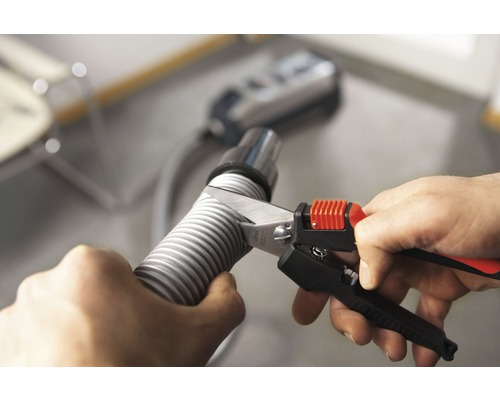 O persoană taie un furtun de aspirator cu o foarfecă pentru furtunuri.