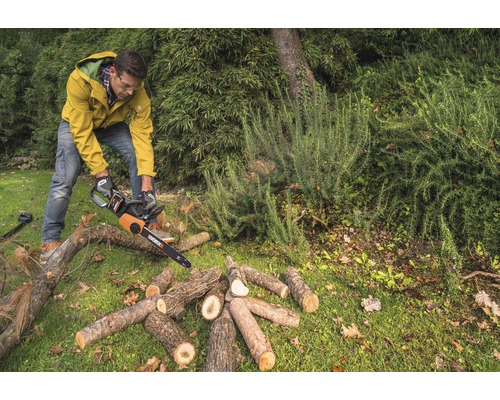Bărbat taie lemne cu un lanț de ferăstrău în grădină.