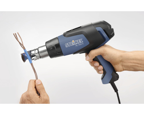 O mână ține un pistol cu aer cald și încălzește un cablu.