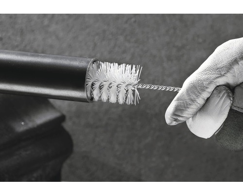 O mână cu mănușă de lucru curăță o țeavă cu o perie de curățare.