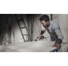 Bărbat taie o placă de lemn cu un ferăstrău circular manual într-un atelier