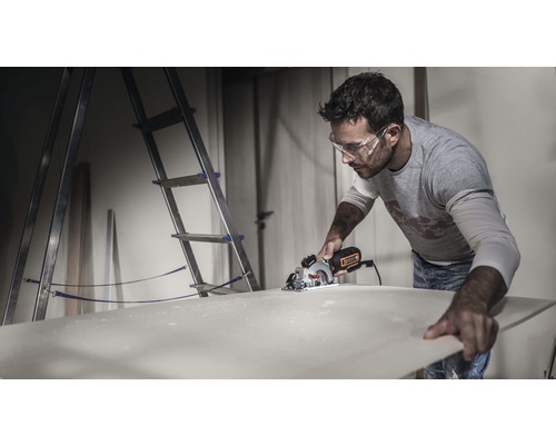 Bărbat taie o placă de lemn cu un ferăstrău circular manual într-un atelier