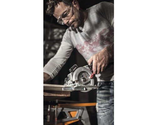 Bărbat taie o scândură de lemn cu un fierăstrău circular manual pe un banc de lucru