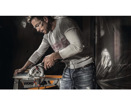 Un bărbat lucrează cu un ferăstrău circular portabil la o piesă de prelucrat pe o masă de lucru marca Worx.