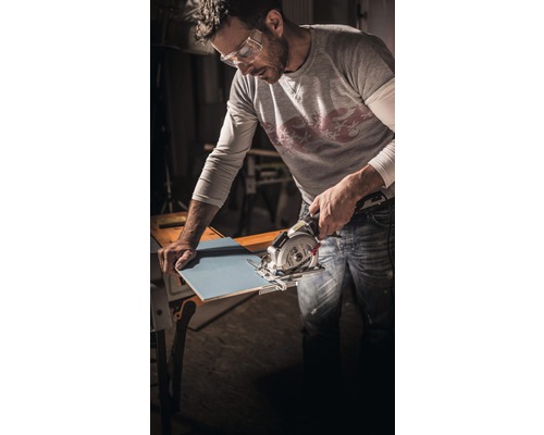 Un bărbat cu ochelari de protecție taie o faianță cu un ferăstrău circular manual.