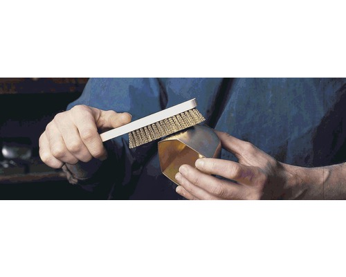 O persoană curăță un obiect auriu cu o perie de sârmă.