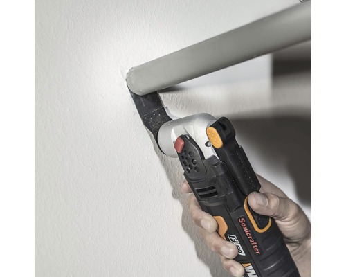 O mână folosește un tăietor multifuncțional pentru a tăia o țeavă pe un perete.