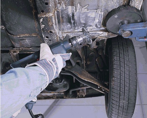 O persoană îndepărtează rugina de pe un vehicul cu o perie de deruginare.