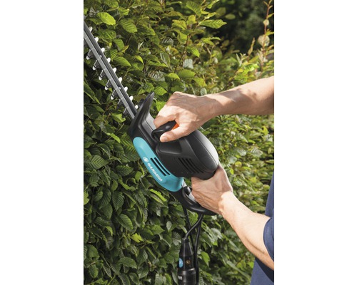 O persoană folosește un gard viu Gardena pe un gard viu.