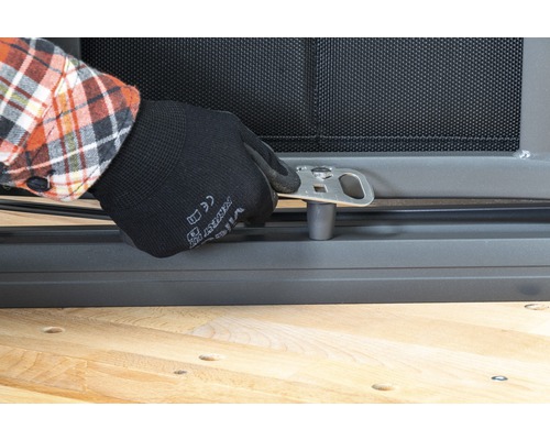 O persoană fixează un suport metalic argintiu de o grilă de fereastră.