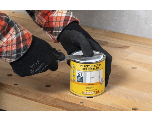 O persoană cu mănuși deschide o cutie de lac acrilic PU pentru ferestre și uși cu o unealtă marca Hornbach.