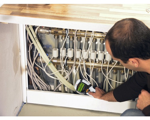 Un bărbat folosește un detector de cabluri pe un colector de încălzire cu țevi și cabluri.