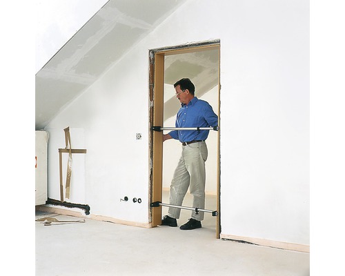 Un bărbat montează un toc de ușă cu distanțiere într-o cameră cu mansardă.