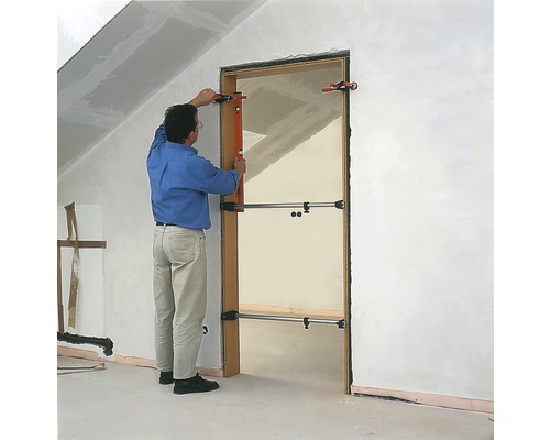 Un bărbat montează o ușă cu un distanțier de ușă într-o clădire în construcție