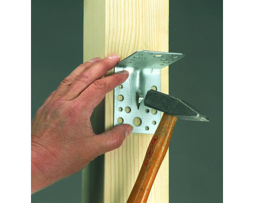 Conectorul de colț este atașat de o grindă de lemn cu un ciocan.