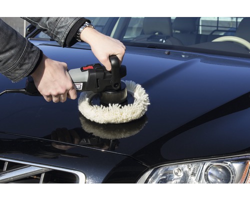 Un bărbat lustruiește capota unei mașini cu o mașină de lustruit.