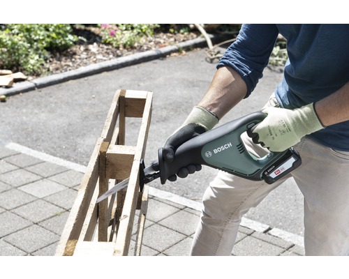 Un bărbat taie un palet din lemn cu un fierăstrău electric cu acumulator